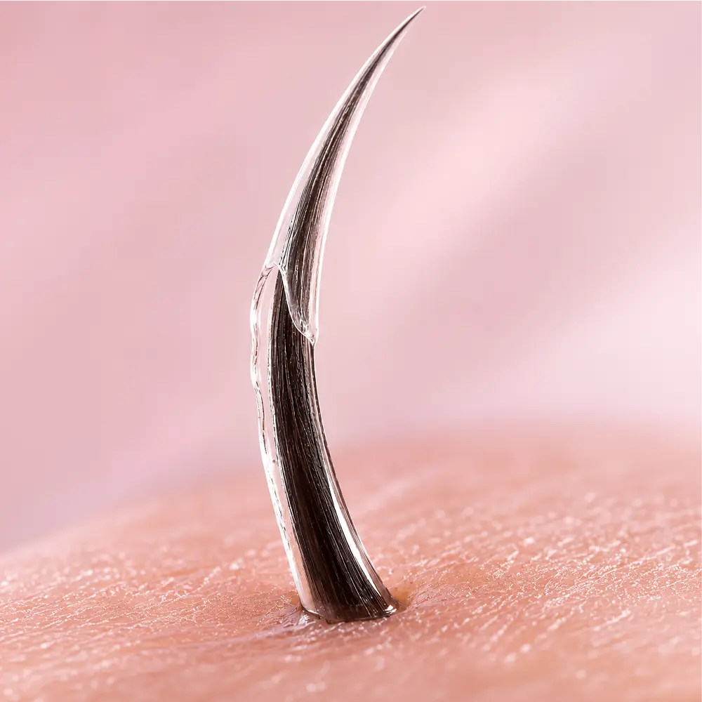 macro on one brow hair, base to tip. The clear film lays down from the base and sets along the shaft in a single pass, then the frame holds on the finished hair. Lit like lab footage, cool and clean. No bottle, no wand, no model in frame.